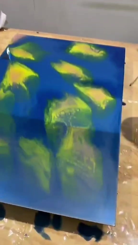 Espelho retangular coberto de azul profundo com manchas amarelas, sobre a bancada do ateliê.